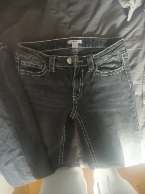 Svarta jeans med vita sömmar Gina Tricot - Säljer ett par svarta jeans från Gina Tricot med tydliga vita kontrastsömmar. Klassisk femficksmodell med knapp och dragkedja framtill samt snygga bakfickor med dekorativa sömmar. Perfekta för en trendig och avslappnad look.