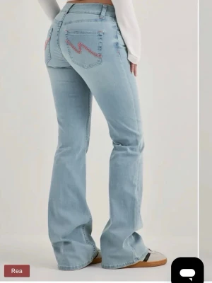Ljusblå bootcut jeans - Säljer ett par ljusblå bootcut jeans med rosa zigzag-broderi på bakfickorna. Inte jätteanvända. Perfekta för en avslappnad och trendig look. Nypris 699