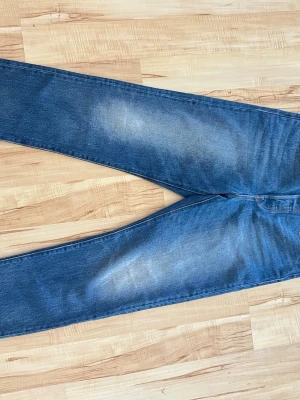 Levi's blå raka jeans med fransig kant - Klassiska blå Levi's jeans med rak passform och snyggt slitna detaljer på låren. Jeansen har en fransig, avklippt benslut och den ikoniska läderlappen bak i midjan. Tillverkade i kraftig denim med fem fickor och röd Levi's-tag på bakfickan.