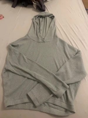 Ljusgrön ribbad hoodie - Mysig ljusgrön hoodie i ribbat material med huva och långa ärmar. Tröjan har en avslappnad passform och är perfekt för en chill och bekväm stil. Inga synliga loggor eller tryck, enkel och stilren design.