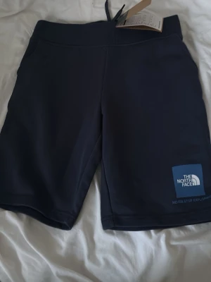 Mörkblå shorts från The North Face - Snygga mörkblå shorts från The North Face med logga på vänster ben. De har en bred resår i midjan och är tillverkade i ett mjukt och bekvämt material, perfekta för sommarens alla äventyr.