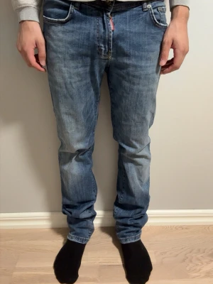 Blå jeans från Dsqaured 2  - Säljer ett par klassiska blå jeans från Diesel med rak passform och fem fickor. Jeansen har snygga slitningar och en ljus tvätt som ger en avslappnad look. Tillverkade i bomull med detaljer i metall och Diesel-logga på bakfickan. Hör av er gällande frågor!!