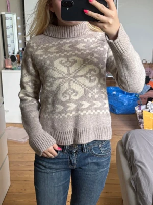 Beige stickad tröja med mönster - Mysig beige stickad tröja med krage och vitt nordiskt mönster framtill. Tröjan har långa ärmar och ribbade muddar vid ärmslut och nederkant. Perfekt för kalla dagar ❣️