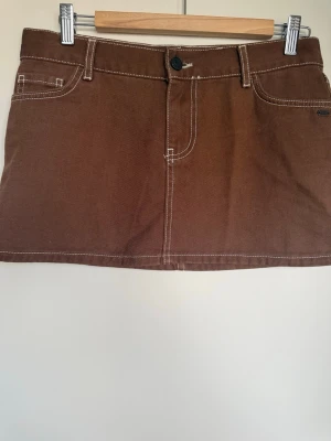 Brun minikjol från Pull & Bear Espania  - Snygg brun minikjol med kontrastsömmar och klassisk femficksdesign. Kjolen har knapp och dragkedja framtill samt två bakfickor.