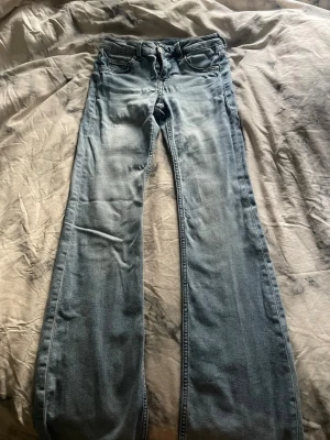 Ljusblå bootcut jeans - Säljer ett par ljusblå bootcut jeans med klassisk femficksdesign och dragkedja. Jeansen har en snygg tvättad look och är tillverkade i mjuk denim som ger en avslappnad vibe. Perfekta för dig som gillar retrostil och vill ha ett par jeans med lite vidare ben. Väl använda men fina ändå