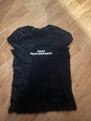 Svart Peak Performance t-shirt - Svart t-shirt från Peak Performance med vit logotyp på bröstet. Klassisk rund hals och korta ärmar. Perfekt för en avslappnad och sportig stil.