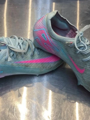Nike Mercurial fotbollsskor elite blå/rosa - Snygga Nike Mercurial fotbollsskor i ljusblått med rosa detaljer och logga. Skorna har en strömlinjeformad design, snörning och greppvänliga dobbar i plast. Ovandelen är i syntetmaterial för bra bollkontroll och lätt vikt. Perfekta för dig som vill sticka ut på planen.