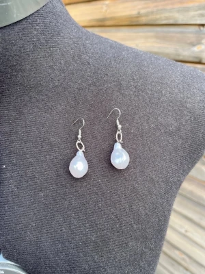 Silvriga örhängen med vita pärlor - Snygga örhängen med droppformade vita pärlor och silvriga krokar. Perfekta för dig som gillar en stilren och klassisk look. Passar till många olika outfits och ger en elegant touch.
