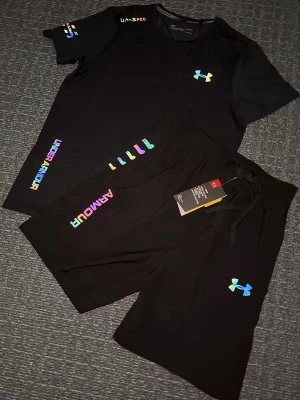 Svart träningsset från Under Armour - Svart träningsset från Under Armour med färgglada loggor och detaljer. Shorts med snörning i midjan och en sportig look, perfekta för träning eller chill. Materialet känns lätt och andas bra. Matcha med t-shirten för en komplett outfit. Storlek S, helt ny 
