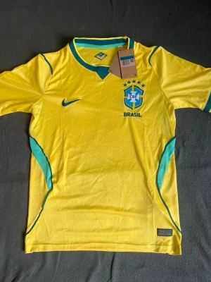 Gul Brasil Nike fotbollströja - Säljer en gul Brasilien fotbollströja från Nike med gröna detaljer och CBF-emblem på bröstet. Tröjan har rund hals med grön kant och är tillverkad i ett lätt, ventilerande material som passar perfekt till träning eller match.