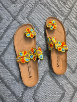 Bruna sandaler med pärlbroderi - Unika bruna sandaler med två remmar och färgglada handgjorda pärlbroderade blommor i gult, rött, blått och orange. Mjuk innersula och svart räfflad yttersula för extra komfort. Perfekta för dig som vill sticka ut med en bohemisk och kreativ stil. Stl är 40 men det kan också passa 39