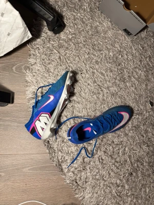 Nike merculiar vapor 16 elite värde 3000kr - Säljer ett par snygga blåa Nike fotbollsskor med rosa och vita detaljer. Bara använda en gång! Storlek 43 värde: 3000kr 
