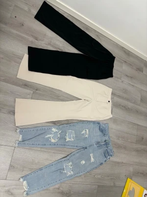 Ljusa slitna mom jeans med hål - Säljer ett par ljusblå mom jeans med flera stora slitningar och hål på framsidan. Jeansen har hög midja, raka ben och fransiga benslut. Perfekta för en avslappnad och trendig look. Jag säljer även ett par svarta kargo byxor som är väldigt stretchiga vid midjan och passar alla storlekar från XS-M. Och jag säljer några flared beiga byxor som inte har använts alls. Både de beiga byxorna och ljusblåa mom jeansen är i storlek S