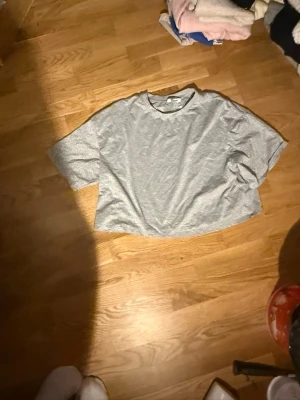 Grå croppad t-shirt - En enkel grå croppad t-shirt med rund hals och korta ärmar. Perfekt för en avslappnad och trendig stil. Tillverkad i mjuk bomull för maximal komfort.