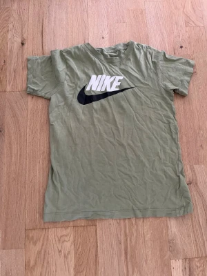 Grön Nike t-shirt med logga - Snygg grön t-shirt från Nike med stor vit och svart logga på bröstet. Klassisk passform och rund halsringning. Perfekt till jeans eller shorts för en avslappnad stil.