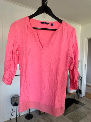 Rosa blus från Tom Tailor - Snygg rosa blus från Tom Tailor med v-ringning och trekvartsärm. Tillverkad i ett lätt och luftigt material som passar perfekt till vår och sommar. Enkel design med bredare kant nedtill för en avslappnad look.