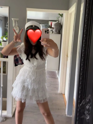 Vit spetsklänning med volanger - Säljer en superfin vit kortklänning med spets och volangdetaljer. Klänningen har korta ärmar och v-ringad hals, perfekt för student eller sommarens fester. Söt och feminin look med flera lager spets och figurnära passform.