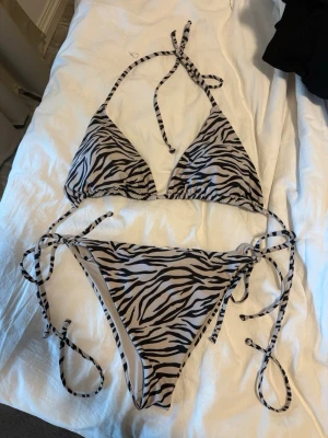 Zebramönstrad bikini med knyt - Snygg bikini med zebramönster i svart och vitt. Överdelen har trekantskupor och knyt i nacken, medan underdelen har knyt i sidorna för justerbar passform. Perfekt för strandhäng eller poolparty.