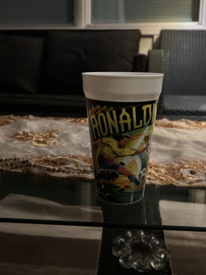 Plastmugg med Ronaldo-motiv - Cool plastmugg med färgglatt tryck av fotbollsspelaren Ronaldinho i action. Muggen har svart, gul, grön och vit design med stjärnor och fotbollstema. Perfekt för dig som gillar fotboll eller vill ha en unik samlarmugg.pris kan diskuteras såklart 