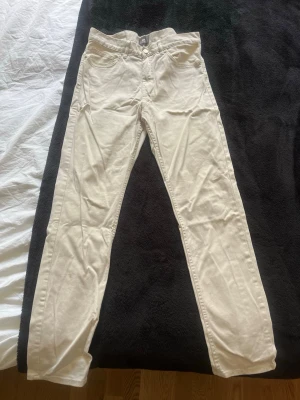 Vita/beige slim fit jeans - Säljer ett par stilrena beiga jeans med slim fit passform och klassiska fem fickor. Jeansen har bälteshällor och stängs med knapp och dragkedja. Perfekta till en avslappnad look och lätta att matcha med olika plagg.