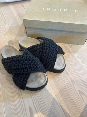 Svarta stickade sandaler Inuikii - Inuikii tofflor i svart. I storlek 39. Är nästintill oanvänd dock har de blivit lite stänk av vatten. Men annars finns inga täcken på användning.