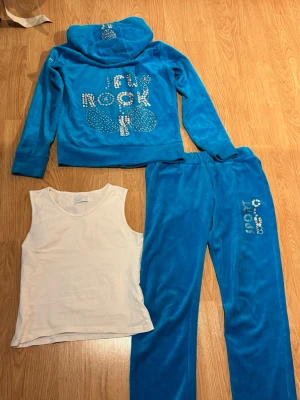Blå tracksuit från J Rock - Blå tracksuit från 2000-talet med glitter detaljer och tjockare material, byxorna är lågmidjade. Alla glitter kristaller sitter på plats och allt ä som nytt!💕 Linnet ingår också. Byxorna är tyvärr för korta för mig!