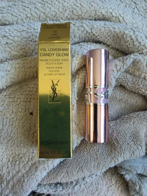 YSL Loveshine Candy Glow Pink Sunrise -  Kommer i en lyxig roséguldig hylsa med YSL-logga och en guldfärgad förpackning. Ger en skimrande, lätt rosa ton och vårdar läpparna med en mjuk, glansig finish.