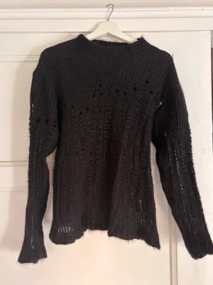 Svart stickad tröja Ann Demeulemeester - Cool svart stickad tröja från Ann Demeulemeester med oversize passform och sliten, hålig design. Tröjan är gjord i ett fluffigt material som ger en edgy och unik look. Perfekt för dig som gillar statement-plagg och vill sticka ut.