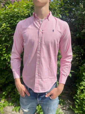Ralph lauren skjorta  - Säljer nu en tvärfet rosarandig skjorta! Storlek 16 vilket motsvarar ungefär M! ‼️OBS‼️ skulle dock säga att den mer S! Personen på bilen är ca 184cm och väger ca 72kg! Hör av er vid minnsta fundering! 