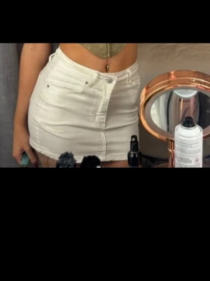 Vit kort jeanskjol  - Trendig vit kort jeanskjol med klassiska fickor fram och bak samt knapp- och dragkedjestängning. Sitter snyggt och har en figurnära passform som passar perfekt till både crop tops och stickade tröjor. Perfekt för dig som vill ha en enkel men stilren look.