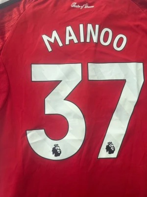 Manchester United matchtröja Mainoo - Röd Manchester United matchtröja 25/26 med Mainoo och nummer 37 på ryggen. Premier League-logga på siffrorna. Tillverkad i lätt och ventilerande material, perfekt för fotbollsträning eller match.