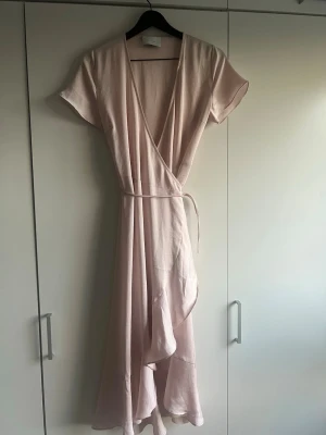Ljusrosa omlottklänning Neo Noir - Säljer en ljusrosa omlottklänning från Neo Noir. Klänningen har korta ärmar, knytband i midjan och en mjuk, lätt textur. Perfekt för dig som gillar en enkel men stilren look med feminina detaljer 💕💕