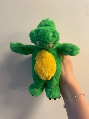 Bolibompa mjukisdjur drake grön - Säljer ett mjukisdjur i form av Bolibompa-draken. Gosedjuret är grönt med en gul mage, vita tänder och svarta klor. Tillverkad i mjukt plyschmaterial och har en klassisk drakform med utstickande armar och ben. Perfekt för alla Bolibompa-fans!