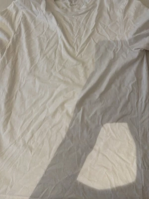 Vit basic t-shirt från H&M - En klassisk vit t-shirt från H&M med rund halsringning och korta ärmar. Tillverkad i mjuk bomull för en skön och enkel stil. Perfekt att matcha med jeans eller shorts för en clean look.