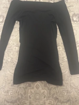 Svart offshoulder topp - Snygg svart offshoulder topp med lång ärm och tight passform. Perfekt för dig som vill ha en enkel men trendig look. Toppen är stilren och passar till många olika outfits. genomskinlig