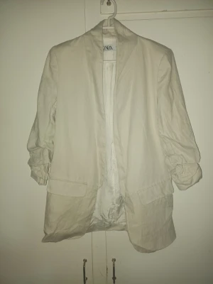 Zara beige blazer i linne-look - Zara blazer i sand/ivory färg. Stilren och oversized modell med uppvikta ärmar och lätt linneliknande material. Perfekt till vår/sommar eller för en clean minimalist look. Använd men i fint skick.