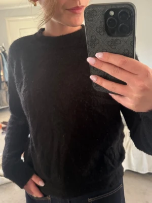 Svart stickad tröja med rund hals - En svart stickad tröja med rund hals och långa ärmar. Tröjan har en enkel och klassisk design, perfekt att matcha med jeans eller kjol. Mjuk och skön stickning som ger en avslappnad look.