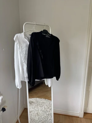 Svart och vit blus med volangdetaljer - Trendig svart och vit blus med långa ärmar och snygga volangdetaljer längs axlarna. Blusen har en lätt, luftig känsla och rundad halsringning. Perfekt att styla med jeans eller kjol för en cool look. Går att köpa båda men också en. 175 för en och 250 för båda💗