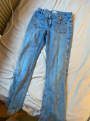 Blå jeans med raka ben från Gina Tricot - Säljer ett par ljusblå jeans från Gina Tricot med raka ben och stora framfickor. Jeansen har klassisk femficksdesign, hög midja och synliga sömmar framtill. Perfekta för en avslappnad och trendig look.
