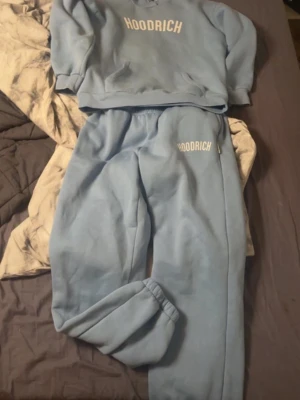Blått loungewear-set från Hoodrich - Mysigt blått loungewear-set från Hoodrich med sweatshirt och matchande byxor. Båda plaggen har Hoodrich-logga framtill. Perfekt för chill dagar hemma. Mjuk och skön bomullsblandning med resår i midjan och vid ärm- och benslut. Byxor i M och hoodie i S