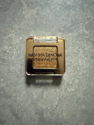 Natasha Denona ögonskugga  - En singelögonskugga från Natasha Denona Golden Palette i en intensivt skimrande guldig nyans. Kommer i en fyrkantig plastförpackning med transparent lock. Perfekt för att skapa en glittrig och iögonfallande look.