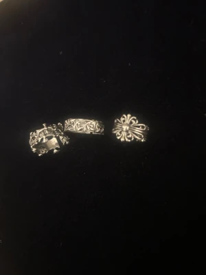 Tre adjustable ÖPPNA silverfärgade ringar med mönster väldigt cool - Säljer tre snygga silverfärgade ringar med detaljerade mönster. En ring har ett kronmotiv, en har blommiga snirkliga detaljer och en har ett stiliserat korsliknande mönster. Perfekta för dig som gillar unika accessoarer med vintagekänsla. SKRIV PÅ öppna ringar passar vem som helst!
