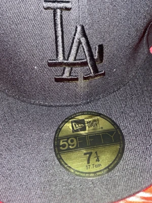 Svart LA-keps från New Era 59FIFTY - Snygg svart keps från New Era 59FIFTY med LA-logga broderad framtill och New Era-logga på sidan. Klassisk flat brim och stilren design, perfekt för dig som gillar streetwear. Tillverkad i slitstarkt tyg och passar dig som vill ha en ikonisk look.