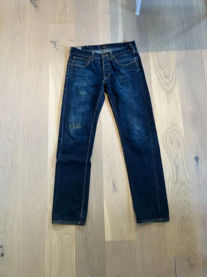  Selvage Lee Darren buttonfly  strl W30 L32 - Säljer ett par mörkblå jeans från Lee med klassisk femficksdesign och slitna detaljer på framsidan, men custom lagning. Jeansen är yellow lable lefthand twill slevage. Jeansen har raka ben och är gjorda i denim med kontrastsömmar. Perfekt för dig som gillar en avslappnad och tidlös look.
