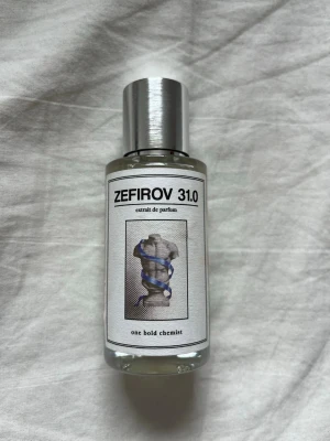 Zefirov 31.0 parfym från One Bold Chemist - Zefirov 31.0 är en parfym i en stilren, genomskinlig glasflaska med silverfärgat lock. Flaskan har en modern etikett med svart text och en konstnärlig bild på framsidan. Perfekt för dig som gillar unika dofter och snygg design. Den är inspirerad av Jean Paul Gaultiers ultra male. Spejad ca 5-8 gånger så är typ helt ny. 