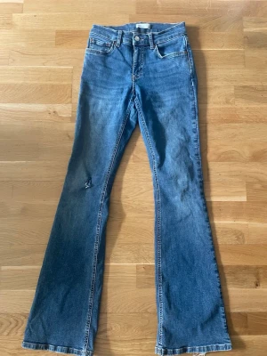 Blå bootcut jeans från Levi's - Säljer ett par klassiska blå bootcut jeans från Gina tricot. Plagget har ett hål på ena knät från en moped krock. Jeansen har mellanhög midja. Plagget är väl använda men är fortfarande i bra skick.