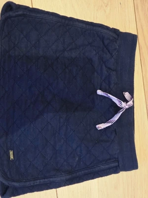 Marinblå quiltade kjol Hampton Republic - Mörkblå kjol från Hampton Republic med quiltat mönster och dragsko i midjan. Kjolen har ribbade muddar och en liten metallbricka framtill. Perfekta för en chill och avslappnad stil.