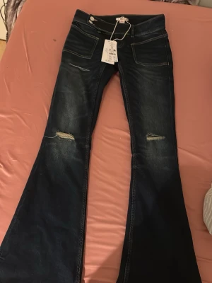 Nya lågmidjade Mörkblå bootcut jeans från Gina tricot  - Säljer ett par mörkblå bootcut jeans från Gina tricot med slitningar på knäna och snygg tvätt. Jeansen har framfickor och markerade sömmar. Perfekta för dig som gillar en retro och avslappnad stil. Lågmidjade helt nya 