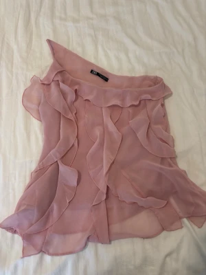 Rosa blus  - Söt ljusrosa offshoulder blus från Zara i ett tunt, transparent tyg med volangdetaljer framtill och längs kanterna. Perfekt för dig som gillar romantisk och feminin stil. Blusen har en luftig passform och är axelbandslös.