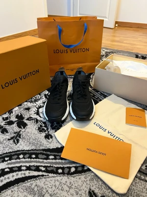Louis Vuitton svarta sneakers - Svarta sneakers från Louis Vuitton med chunky vit sula och detaljer i beige på hälen. Skorna har en modern och sportig design med klassiska LV-detaljer. Materialmix av läder och textil ger en lyxig känsla. Perfekta för dig som vill sticka ut med exklusiva sneakers.
